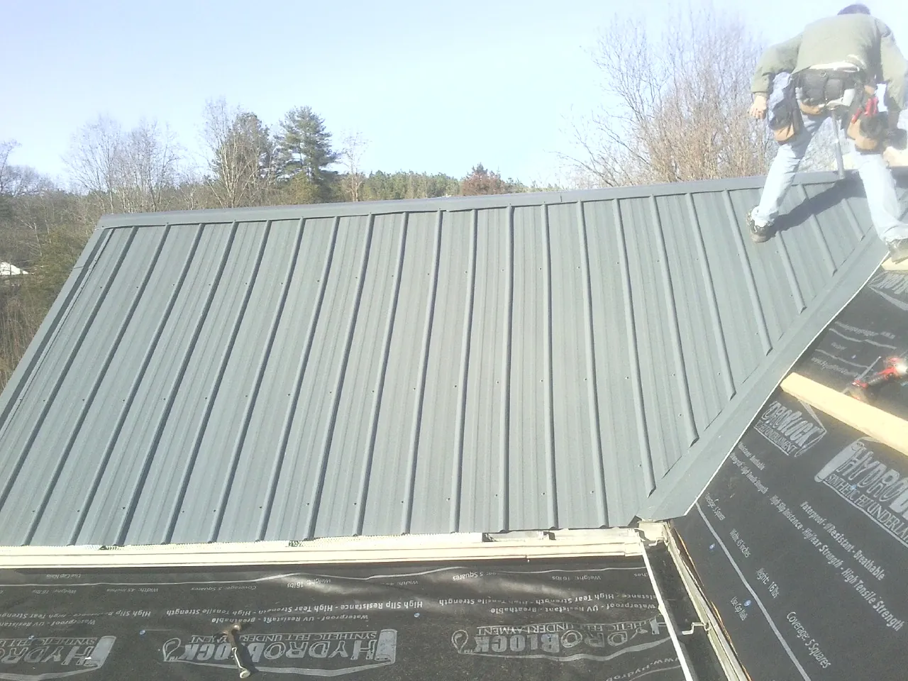 Crew installing dark green standing seam panels over synthetic underlayment in Stockton